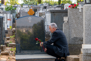 Mature man in black clothes on cemetery, holding a flower and mourning for family loss. Concept for...