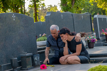 Mature couple in grief, in black clothes, holding a flower and mourning a deceased loved one on...