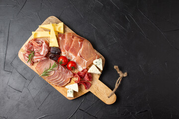 Mixed delicatessen with charcuterie and cheese board with a place for text. Italian appetizers or antipasto set with gourmet food on dark background