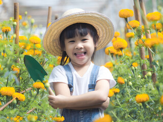 Cute little girl in hat holding garden tool shovel for planting flowers in the garden. A child helps mom in the garden, a little gardener.