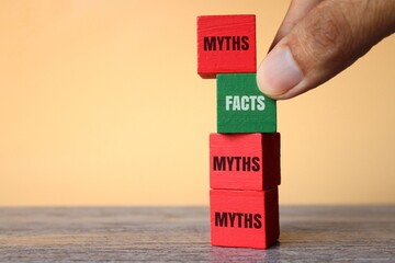 Hand pick wooden cube with text FACTS over MYTHS. Facts vs myths concept.