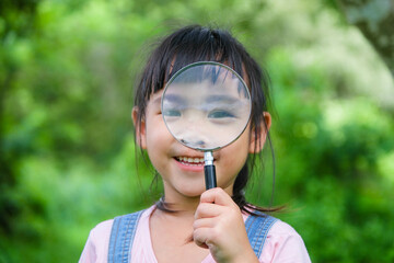 Cute little girl learning and exploring nature with outdoor magnifying glass. Curious child looks through a magnifying glass at a tree in the park. Little girl playing with a magnifying glass.