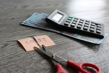 Scissor, calculator, money and note with text COST. Financial, cost cutting, reduce expenses concept