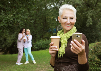 Beautiful old blond woman laughing, holding a cup of coffee to go, take selfie and feeling so happy.