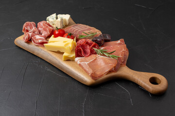 Mixed delicatessen with charcuterie and cheese board with a place for text. Italian appetizers or antipasto set with gourmet food on dark table