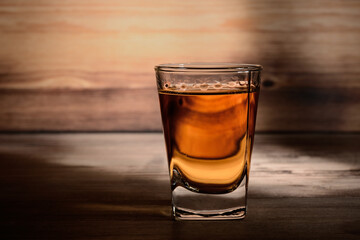 Shot glass of aged alcohol, close-up on a wooden table and against a background of a wooden unfocused texture