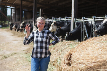 A contented adult woman stands next to cows on a farm.