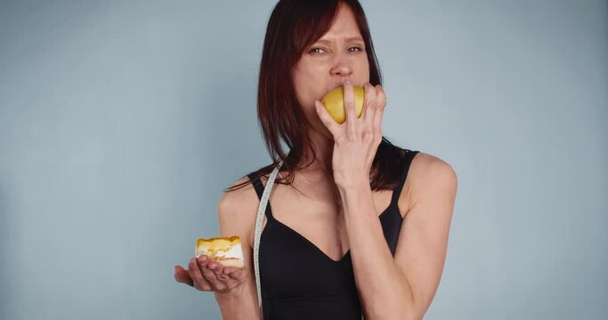 Young woman chooses apple instead of cake. Static studio video
