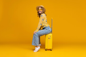 Fototapeta na wymiar smiling woman traveling with suitcase dressed in trendy outfit on bright yellow background, positive summer vacation