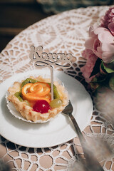 Fruit dessert on the newlyweds table. Grapes, orange, kiwi, cherry in a plate. Nearby lies a bouquet of pink flowers.