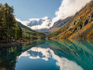 Picturesque mountain lake in the summer day, Bright sunny landscape with glacier reflection in water surface of mountain lake under clear sky. Beautiful reflection of mountains, sky and white clouds