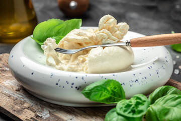 Creamy Italian Burrata Cheese with basil, olive oil on white plate on wooden background. banner, menu, recipe place for text
