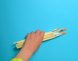 child holding brushes for painting on a blue background