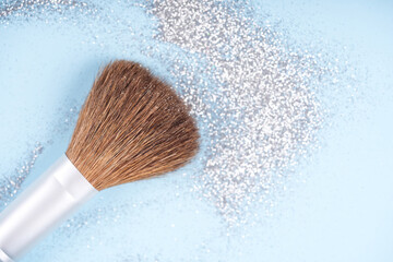 Festive holiday or Christmas makeup concept. Makeup brush over pastel blue background with silver sparkles and glitter around. Template with copy space for text
