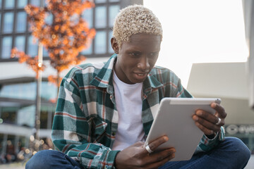 Young smiling African American student using digital tablet studying, learning language sitting in...