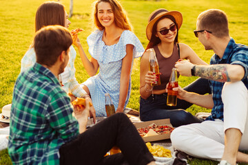 group of friends are enjoying pizza in the park. Men and women sit on the grass around a pizza box