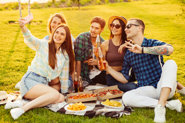 Happy friends have a picnic in the city park outdoors. Friends have fun talking and taking selfie on mobile phone