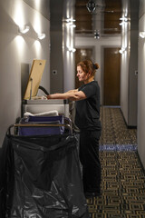Cleaners trolley with cleaning equipments and housekeeper at hotel in hallway. Cleaning cart with...