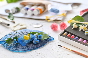 Leisure. Hobbies and recreation. Creating flowers and ornaments from cold porcelain. Painting of jewelry. Different flowers and decorations close-up next to pastel crayons and other tools of master