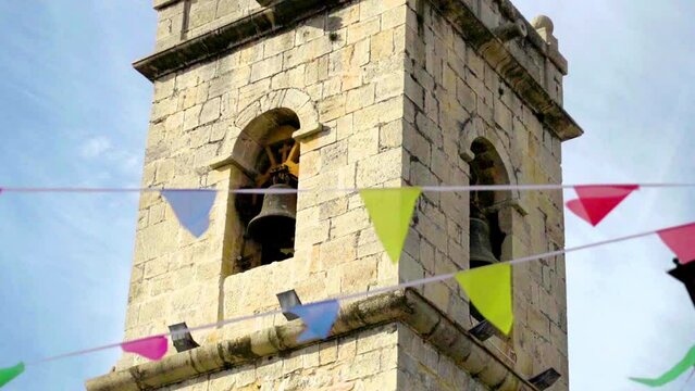Slow motion. Town bell tower, on a sunny day with colored festive flags.