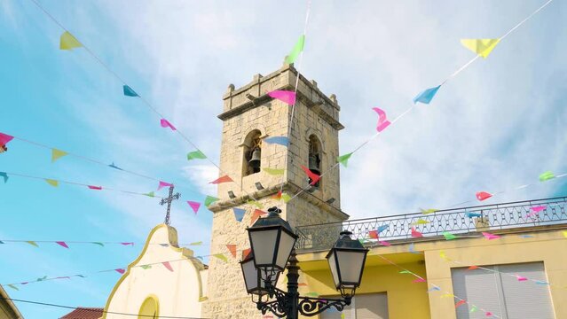 Lamppost with festive flags hanging, with the bell tower of the town behind