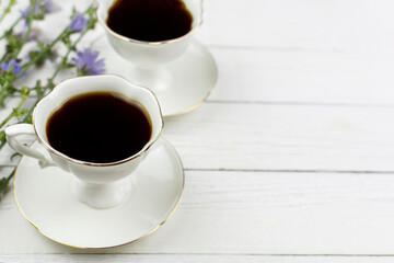 Two cups on saucers with a chicory drink on a white wooden background. Place for the text, ingredient, recipe. A useful substitute for coffee.