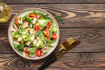 Fresh salad with vegetables and fish. Arugula, spinach, cucumbers, tomato, onions and fish in a plate on the table. Diet nutrition. Top view. Copy space