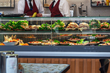 Glazed showcase inside a cafe with fresh Italian dishes and herbs in Milan, national Italian cuisine for fast food, behind the showcase a couple of uniformed waiters