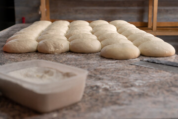 On the table there is a lot of prepared dough for baking buns or other bakery products, a container with flour and a knife-cutter for dough