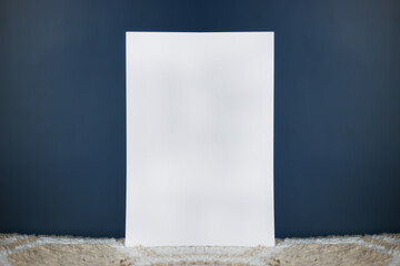 A white sheet of paper stands vertically on a light carpet and an isolated dark background