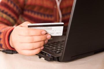 Woman wearing a sweater, holding a credit card and lokking her black laptop 
