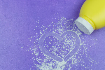 Scattered from a yellow bottle of dry white baby powder under a diaper on a lilac (purple) background. Drawing a finger on the children powder in the form of a heart. Space for text.