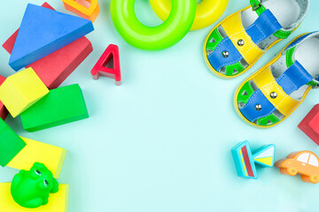 Multi-colored constructor, red cubes, green rubber frog, summer sandals (shoes), figures for sorter, pyramid rings on a blue background. Space for text. Children's background. Baby toys.