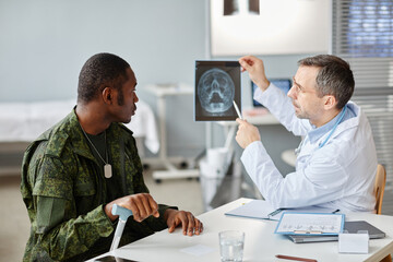 Professional medical worker showing skull x-ray picture to young adult military officer during...