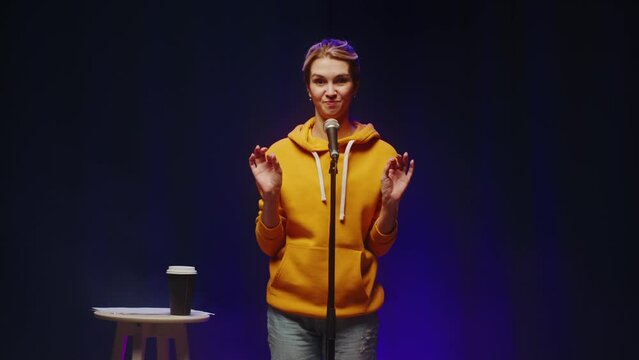 Stand-up cafe, woman comedy concert. Woman telling jokes on stage. Female comedian speaking with audience using microphone, humorous monologue. Mentor coach training.