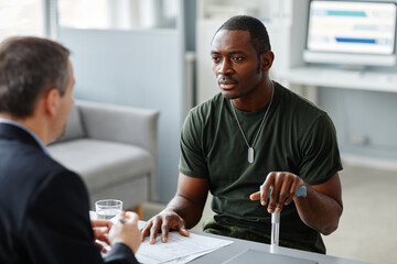 Young adult African American soldier with walking stick talking about his problems to psychologist during individual therapy session - obrazy, fototapety, plakaty