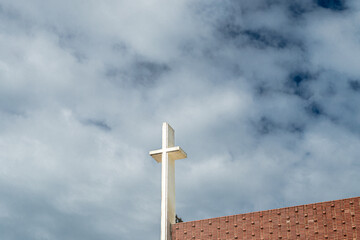 Detail of a white concrete cross on cloudy sky.