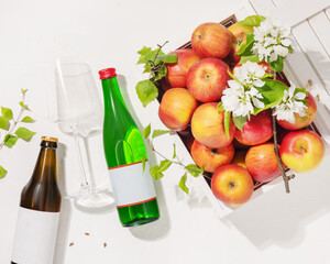 Bottles of natural apple cider with wine glass and farm apples in a white wooden box on a white background. Summer Refreshing Low-alcohol fruit drink. Apples product. Soft focus style, flat lay
