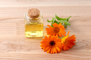 Bottle of essential oil and calendula flowers on a wooden table. - obrazy, fototapety, plakaty
