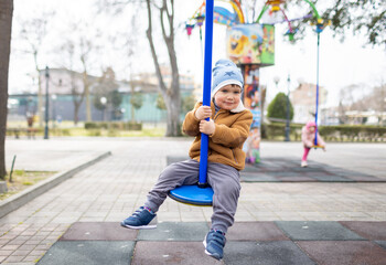 A boy on a playground in an autumn park rides on a swing in cloudy weather