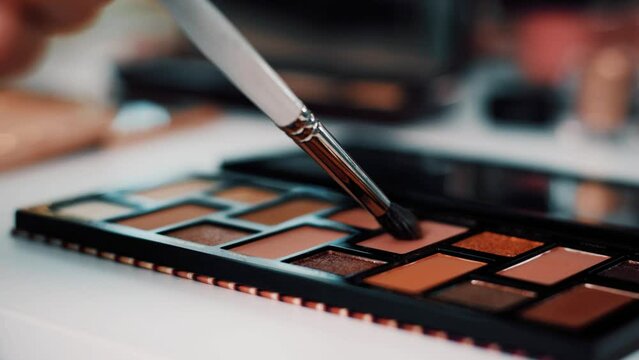4K cinematic close-up video of eyeshadow brown colour palette. Cosmetic brush touching different colours of shadow.