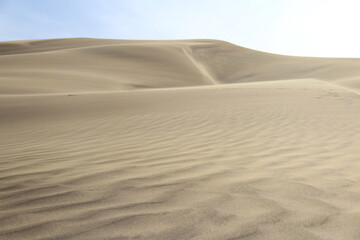 Large sand dune with several peaks against the sky in sunlight, beautiful sandy waves on the slopes, singing dune, summer