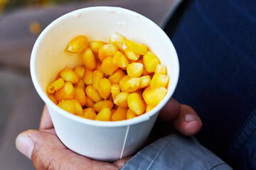 hand holding a paper cup with boiled sweet corn