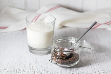 Yogurt or kefir and flax seeds in a small glass jar on a white kitchen table.