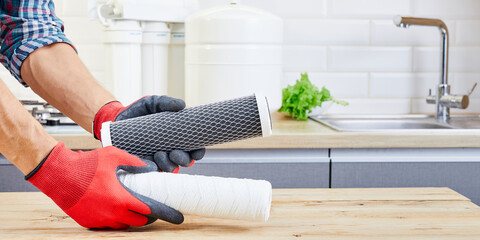 Hands holding a filter cartridge of domestic drink water treatment systems at kitchen background. Aqua filter cartridge in human hand.