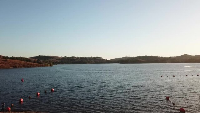 gorgeous footage of a vast rippling blue lake at sunset surrounded by majestic mountain ranges covered in lush green trees and plants with blue sky at Puddingstone Lake in San Dimas California USA