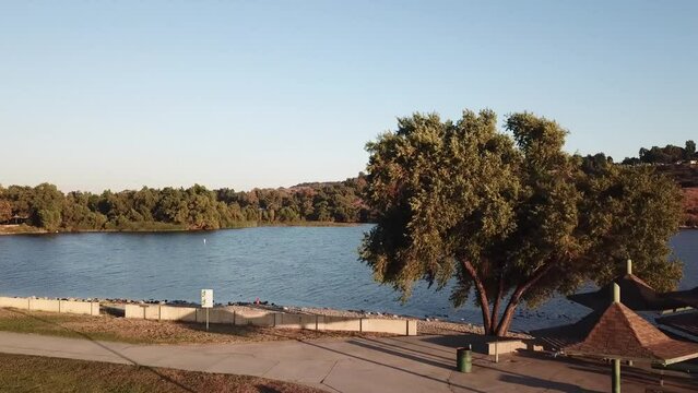 gorgeous footage of a vast rippling blue lake at sunset surrounded by majestic mountain ranges covered in lush green trees and plants with blue sky at Puddingstone Lake in San Dimas California USA