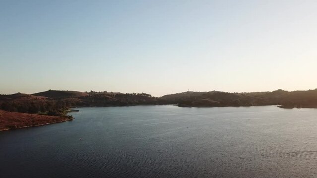 gorgeous footage of a vast rippling blue lake at sunset surrounded by majestic mountain ranges covered in lush green trees and plants with blue sky at Puddingstone Lake in San Dimas California USA