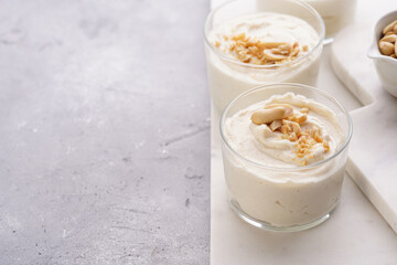 Creamy dairy yoghurt dessert with mascarpone, cream cheese and peanut butter in glasses on marble tray, copy space