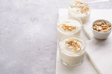 Creamy dairy yoghurt dessert with mascarpone, cream cheese and peanut butter in glasses on marble tray, copy space